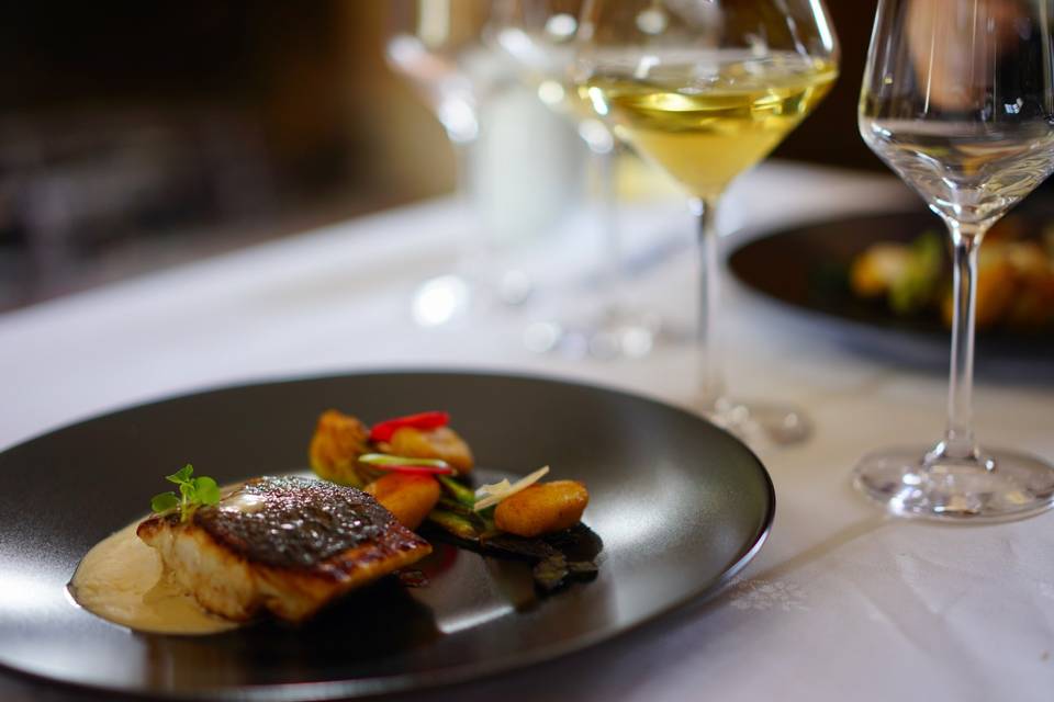 Un plato de la cena, pescado y verduras, con una copa de vino blanco